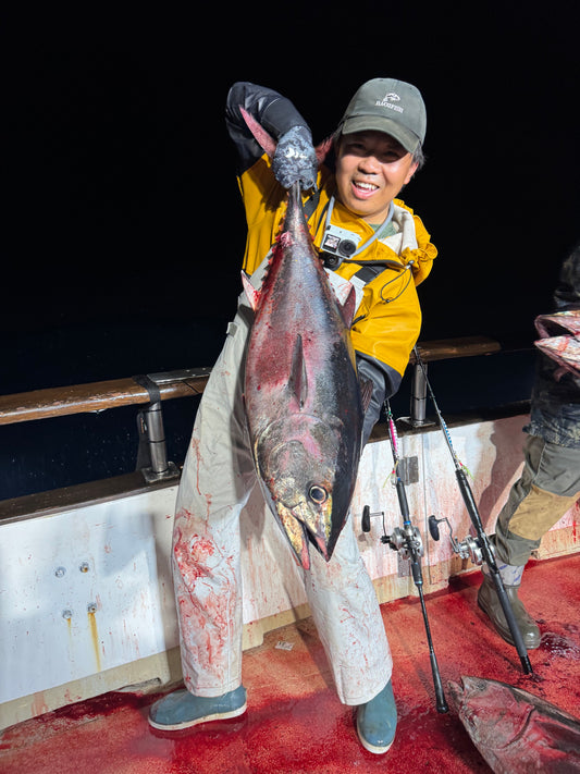 Angler on deck at night holding a tuna